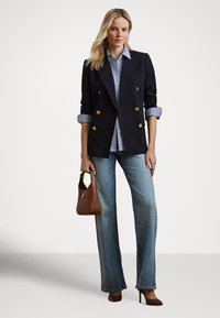 Blazer azul-marinho de abotoamento duplo com botões dourados, camisa às riscas, jeans azuis claros com bainha alargada, mala castanha e sapatos de salto combinando. Texturas suaves.