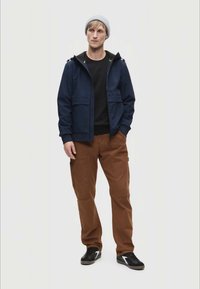 Marinehættejakke, sort skjorte, brune cargo bukser og sorte sko. Beanie-hat. Casual outfit med lommer på bukserne og hætteaccenter.