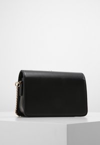 Borsa in pelle nera con una texture liscia, forma rettangolare e tracolla in catena dorata. Presenta una chiusura a pattina e dettagli minimi.