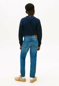 Sudadera azul marino y jeans de color azul claro con un parche de cuero. El modelo lleva zapatillas beige y muestra un diseño de tela texturizada.