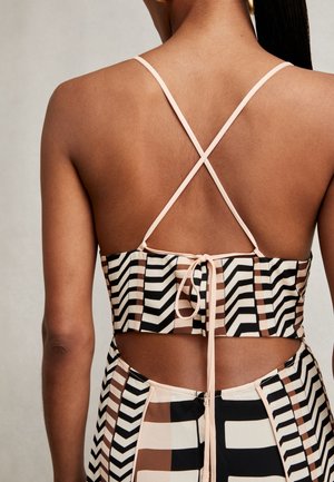Žena u bezrukom, otvorenom topu s križnim tankim trakama i geometrijskom suknjom u crnoj, bijeloj i smeđoj boji.