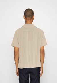 Camicia beige a maniche corte con strisce verticali bianche e colletto appuntito, caratterizzata da un tessuto strutturato e una vestibilità comoda.