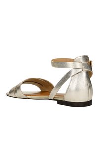Metallic silberne flache Sandale mit offenem Rücken, überkreuzten Riemen, einer weichen Innensohle und einer niedrigen schwarzen Sohle. Strukturiertes Leder.