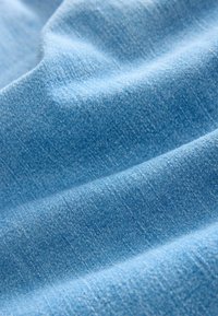 Helleblaue Denim-Stoff mit einer samtigen Textur, der subtile Farbvariationen aufweist und ein glattes, leicht zerknittertes Aussehen zeigt.