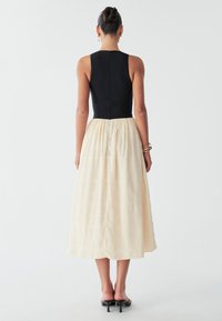 Black knit bodice with back zipper, cream pleated skirt, below calf length, smooth texture, worn with black heeled sandals.