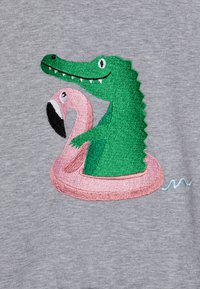 Design ricamato che presenta un coccodrillo verde e un fenicottero rosa su un salvagente in uno sfondo grigio melange.