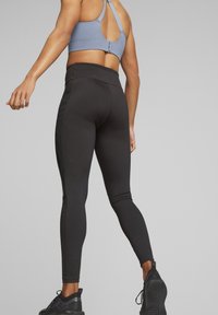 Leggings neri a vita alta con pannelli laterali, abbinati a un reggiseno sportivo azzurro chiaro con schiena bassa e spalline incrociate. Tessuto testurizzato.