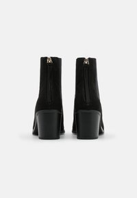 Stivaletti alla caviglia in pelle scamosciata nera con chiusura a zip, caratterizzati da un tacco affusolato e una finitura liscia e testurizzata. Design semplice senza motivi visibili.