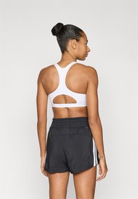 Λευκό αθλητικό σουτιέν με σχεδιασμό racerback, που διαθέτει λεπτομέρεια σε σχήμα κοψίματος· συνδυασμένο με μαύρο σορτς με ελαστική μέση και πλευρικές ρίγες.
