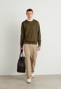 Pull à manches longues vert olive, pantalon beige, col de chemise blanc, portant un sac noir, assorti avec des baskets blanches.