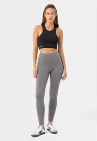 Černý crop top a šedé legíny s vysokým pasem vyrobené z elastického materiálu. Výrazné logo na obou kouscích, doplněné o černobílé tenisky.