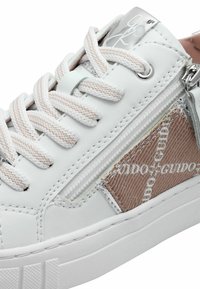Baskets blanches avec un panneau latéral texturé, dotées d'une fermeture éclair, de lacets contrastants et d'une semelle en caoutchouc. Accents argentés sur la languette.