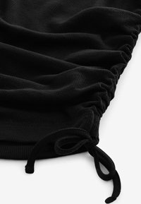 Crna rebrasta tkanina s nabranom teksturom i detaljem na uzici. Materijal izgleda mekano i rastezljivo, što poboljšava udobnost i prilagođavanje.