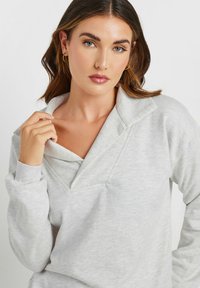 Felpa grigia chiara con colletto pieghevole, caratterizzata da una finitura testurizzata, maniche lunghe e una vestibilità comoda. Dettaglio del design a V molto evidente.