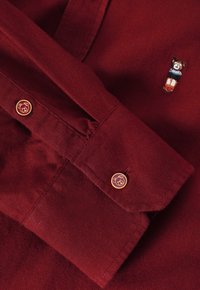 Bordeaux skjorte med broderet bjørnemotiv og brune knapper med bjørne-design. Blød stofstruktur med struktureret krave og manchetter.
