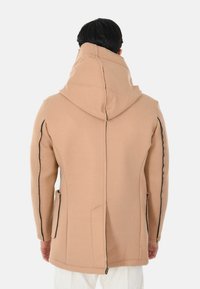 Cappotto beige con cappuccio dal design essenziale, tasche laterali, cuciture nere a contrasto e finitura del tessuto strutturata.