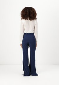 Šviesiai mėlynos plačios kelnės su išpjovomis, aukštu liemeniu ir lygia medžiaga. Derinamos su šviesios spalvos ilgomis rankovėmis palaidine.