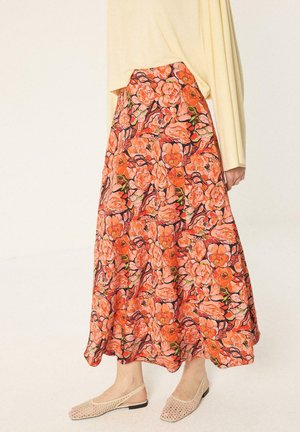 Longue jupe fleurie dans des tons orangés et roses portée avec un haut crème et des chaussures slingback beiges à talons bas.