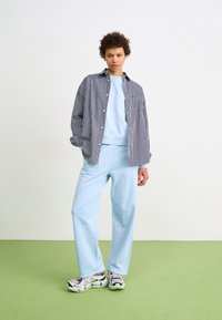 Un sweat-shirt bleu clair et un pantalon de survêtement assorti avec une coupe décontractée, superposés sous une chemise à rayures noires et blanches à boutons. Des baskets complètent le look.
