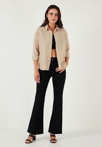 Bežena košulja s dugim rukavima, crni crop top, crne široke hlače i crne sandale na remenčiće. Glatka tkanina i lijepo krojen fit, u stojećem Odsjeku.
