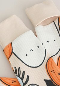 Pletené bavlnené ponožky s pastelovo ružovými rebrovanými manžetami. Obsahujú farebné abstraktné tváre a kvetinové vzory na béžovom pozadí.