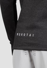 Felpa grigio scuro con tessuto testurizzato, caratterizzata da un logo bianco "MOROTAI" in basso e cuciture lisce lungo i bordi.