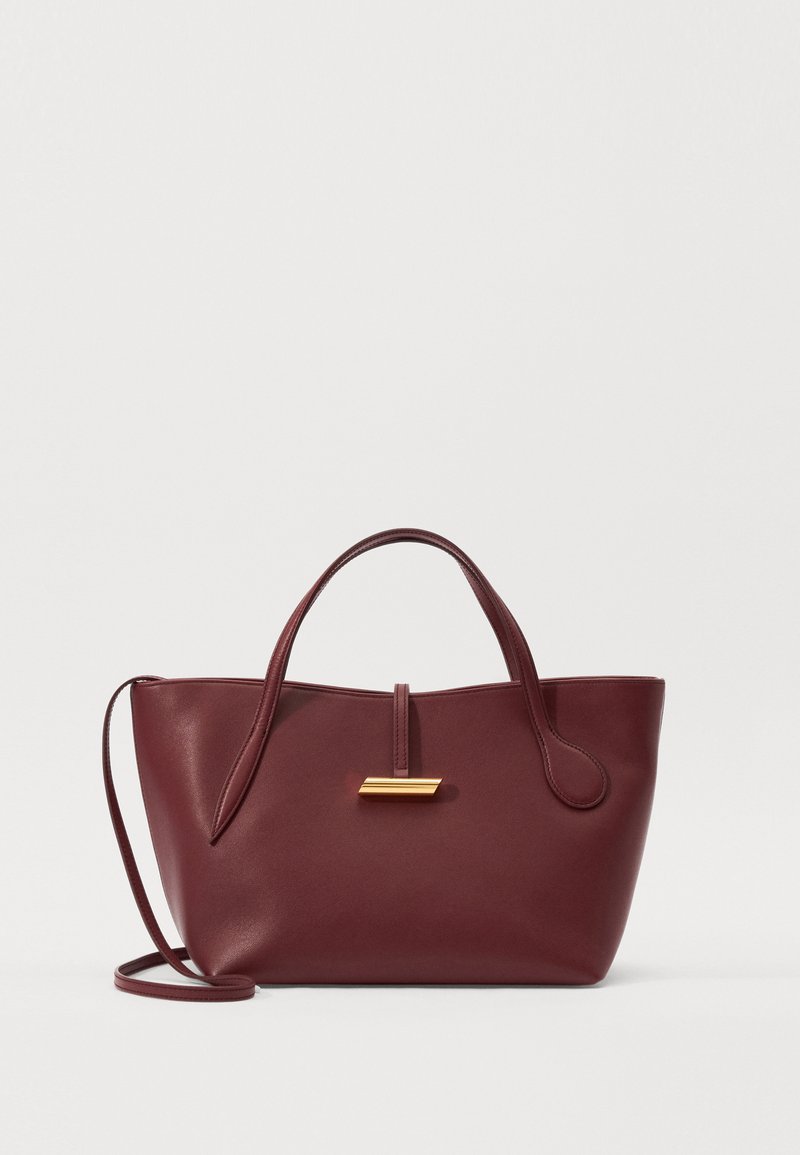 Bordo ādas rokas soma ar elegantu siluetu, divām rokturām un noņemamu plecu siksnu. Priekšpusē ir zelta tonī akcenti.