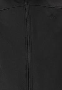 Tissu noir avec fermeture éclair centrale et logo triangulaire embossé subtil en haut à droite.