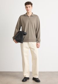 Világos barna pulóver fél cipzárral, amely off-white széles lábú nadrággal és fekete bőrcipővel van párosítva, egy fekete táskával.