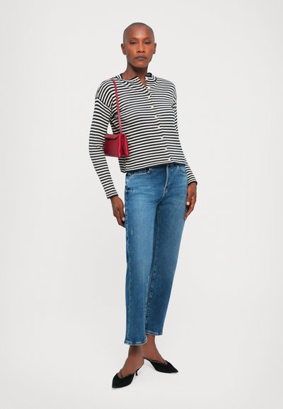 Schwarz-weiß gestreiftes Hemd mit Knöpfen, blaue Jeans, schwarze spitz zulaufende Schuhe und eine kleine rote Handtasche. Klare Details und Texturen sichtbar.