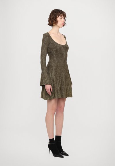 Geribbelde, metallic gouden jurk met een aansluitend lijfje, uitlopende mouwen en een geplisseerde rok; gecombineerd met zwarte hoge laarzen.