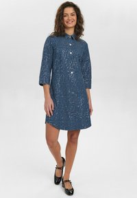 Abito in denim blu con colletto, maniche a tre quarti, chiusura con bottoni e una superficie testurizzata decorata con paillettes metalliche.