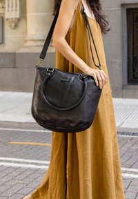 Musta nahast õlakott ümmarguste käepidemete ja eemaldatava rihmaga. Kotil on sile tekstuur ja minimalistik disain.