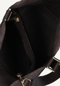 Donkerbruine leren handtasinterieur met textuurvoering, een centrale met rits gesloten pocket en metalen sluitingen en gespen op de strap.