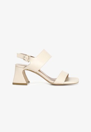 Beige leather sandal with two wide straps, an ankle buckle, and a block heel. Smooth texture with a rounded open toe design.