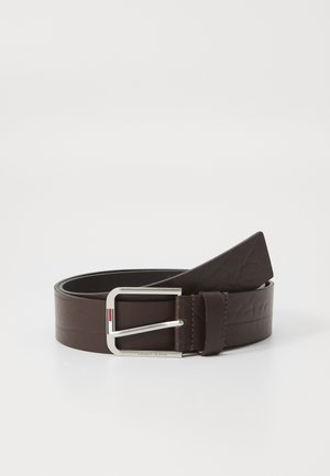 Smeđi kožni pojas sa jednostavnom srebrnom metalnom kopčom. Ima urezanu teksturu i šivani rub, s brendiranjem "TOMMY JEANS" na kopči.