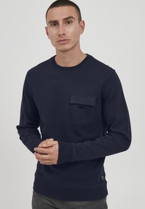 Felpa blu navy con scollo rotondo e maniche lunghe, dotata di taschino sul petto. Realizzata in morbido tessuto con orlo e polsini a costine.