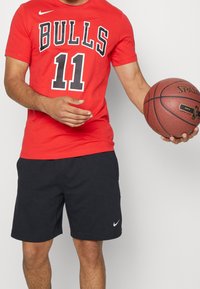 Red cotton t-shirt with "BULLS" and "11" printed in black. Paired with black shorts featuring a white Nike logo. Holding a brown basketball.