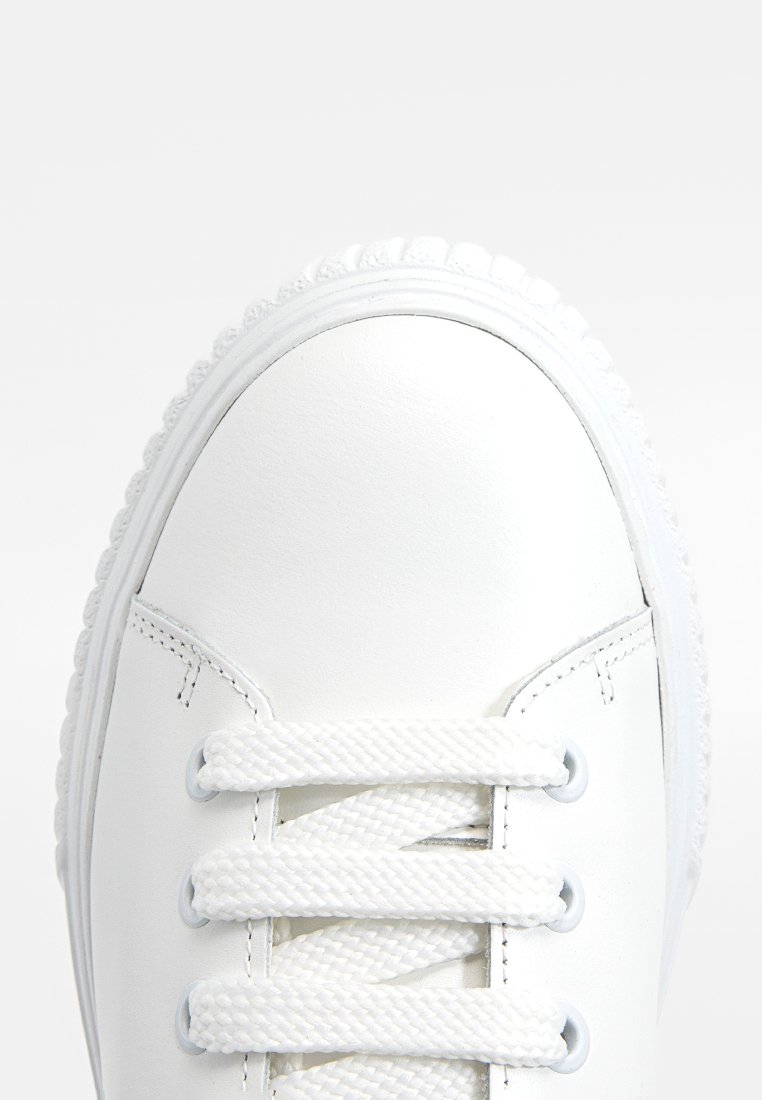 Weißes Leder-Sneaker mit runder Zehenpartie und strukturiertem Sohlenprofil. Verfügt über flache weiße Schnürsenkel und Metallösen, die eine glatte Oberfläche mit minimalen Akzenten zeigen.