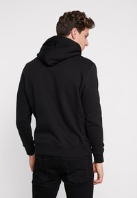 Zwarte hoodie met een relaxed fit, geribbelde manchetten en onderzoom, en een zachte stoftextuur. Bevat een kangoeroezak aan de voorkant.