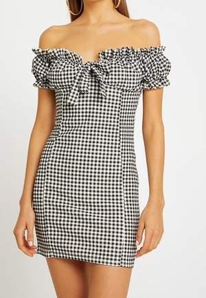 Kvinde iført en sort-hvid gingham minikjole med bare skuldre, puffede ærmer og bindedetalje foran.