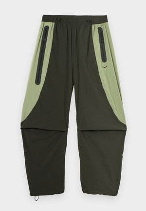 Zelene in črne športne hlače ohlajenega kroja, z dvema stranskima žepoma na zadrgo in elastiko v pasu. Lahka, gladka tkanina.