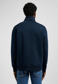 Sweat à col montant bleu marine, avec des poignets et un ourlet côtelés, fabriqué à partir d'un tissu doux, offrant une coupe décontractée et un design minimaliste.
