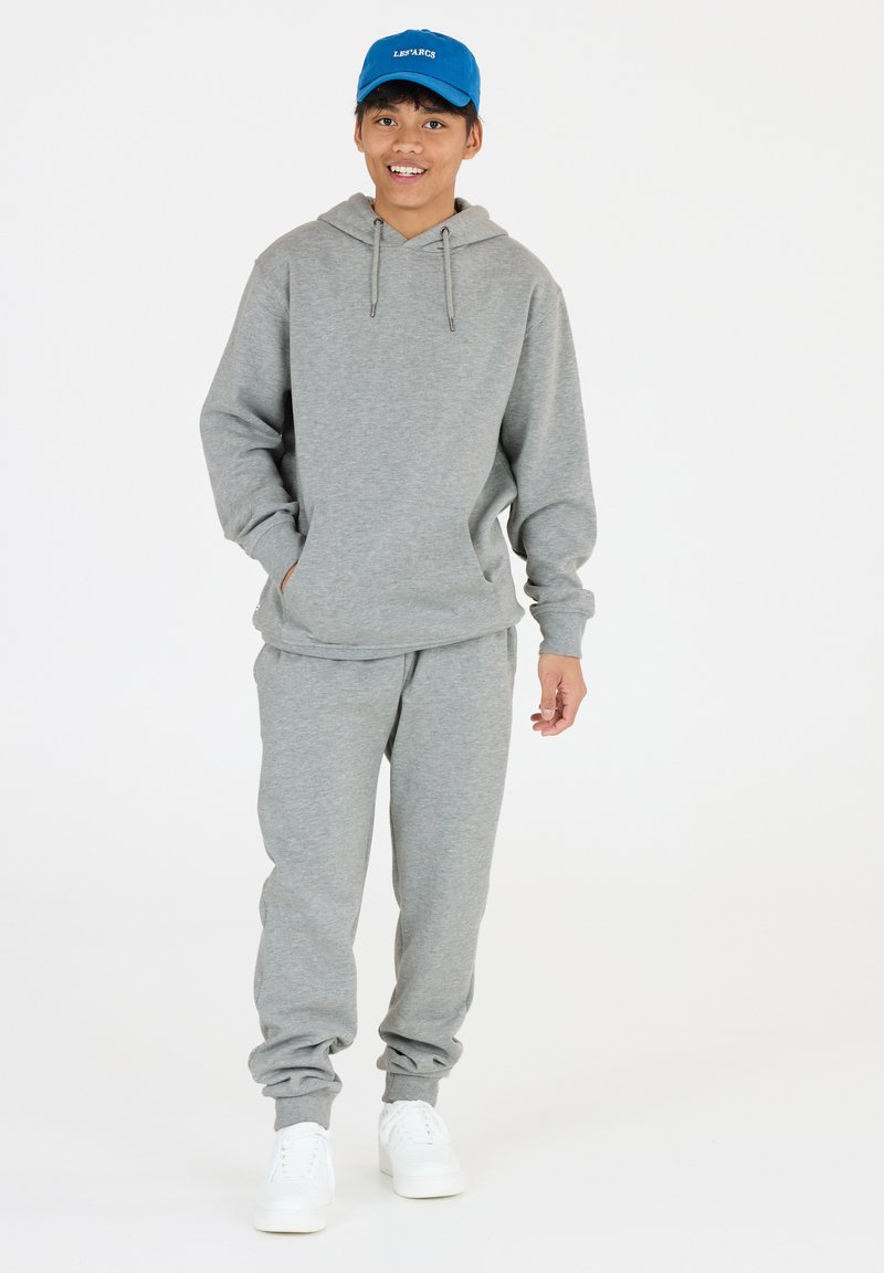 Grijze hoodie met trekkoord, gecombineerd met grijze joggingbroek. Bevat elastische manchetten en een elastische tailleband. Draag het met witte sneakers en een blauwe pet.