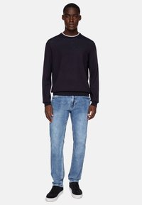Dark navy sweater with a light-colored crew neck, paired with light blue jeans and black sneakers. The sweater has a textured finish.