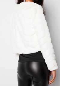 Hvid, tekstureret kunstpelsjakke med quiltet design og rund halsudskæring, båret over en sort top og sorte leggings med læderlook.