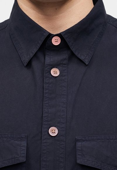 Σκούρο μπλε πουκάμισο με ροζ κουμπιά κουμπωμένα, με κλασσικό γιακά και δύο τσέπες στο στήθος.