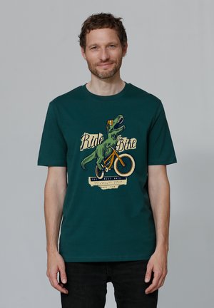 Dark green cotton t-shirt featuring a graphic of a dinosaur on a bicycle. Text reads "Ride Bike" with notable vintage design elements.