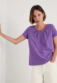 Camiseta corta de manga corta de color púrpura con un cuello redondo y un detalle de abertura, y tejido fruncido en la parte delantera, de textura suave.