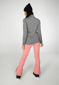 Enganliegender grauer Langarmshirt mit einem Stehkragen, kombiniert mit pinkfarbenen Schlaghosen und schwarzen Schneestiefeln, von hinten betrachtet.